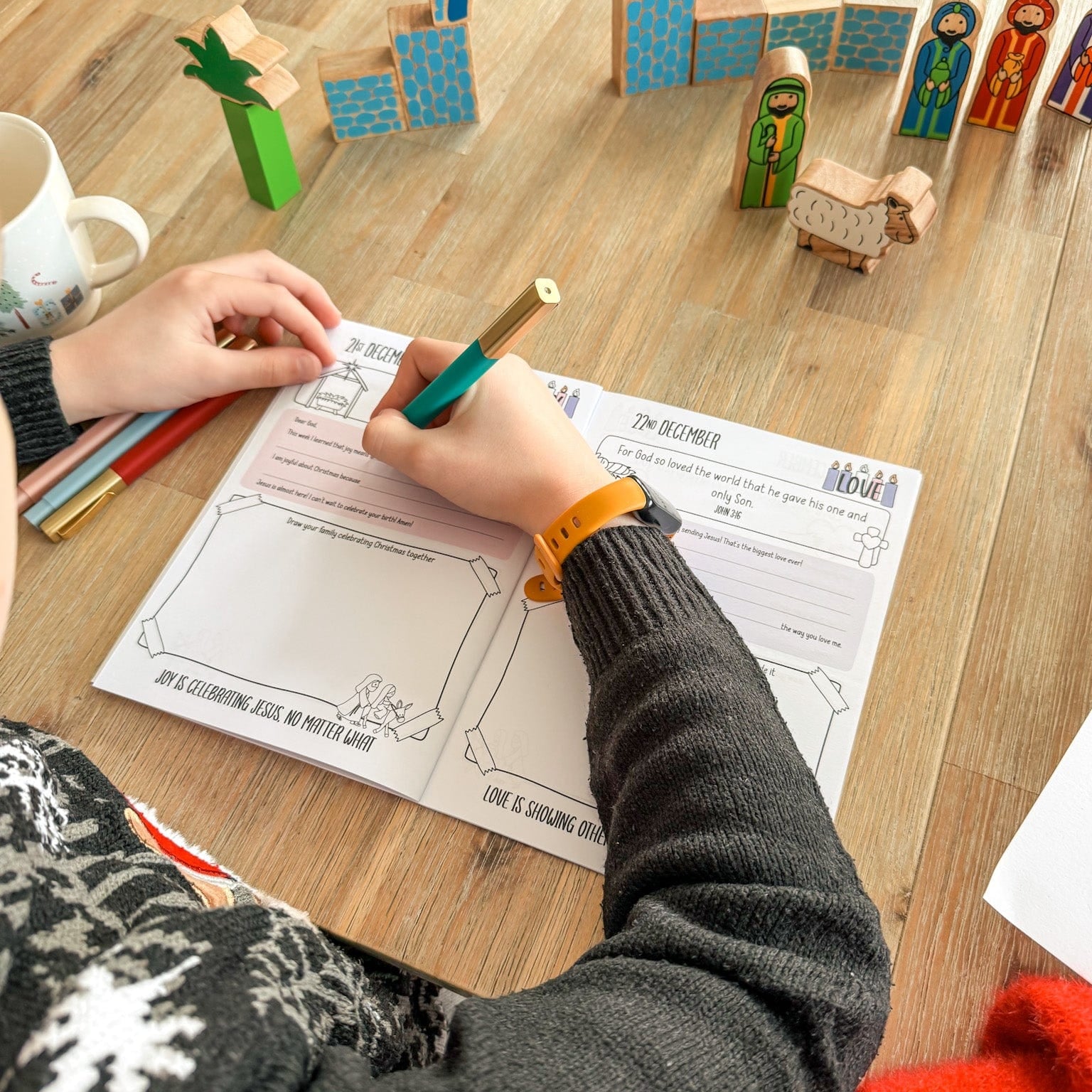 A child filling in his advent journal surrounded by a wooden nativity scene