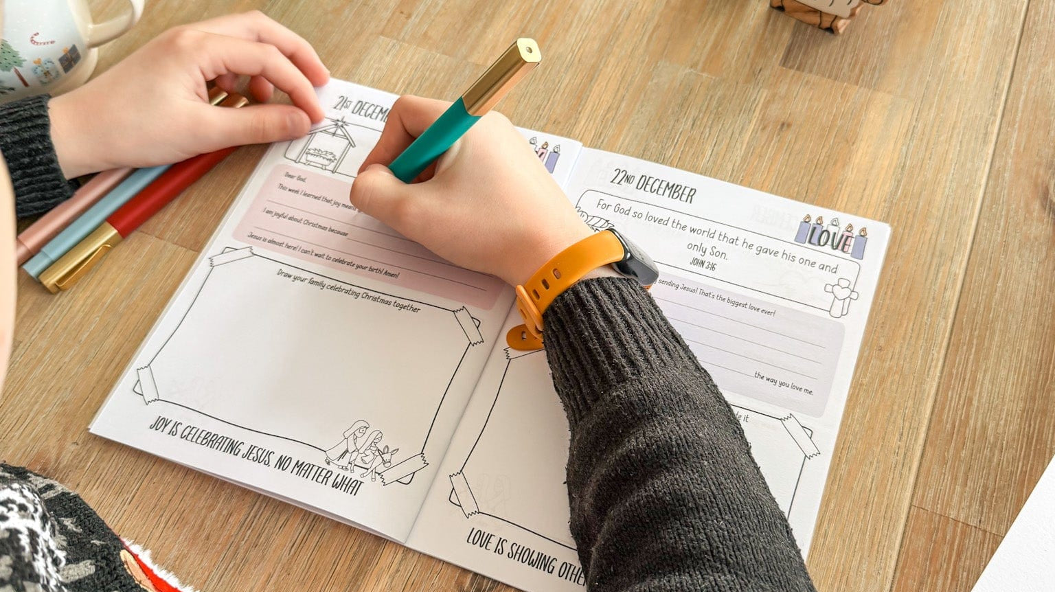 A child filling in his advent journal surrounded by a wooden nativity scene