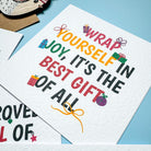 Holiday-themed card with text 'Wrap yourself in joy, it's the best gift of all. Santa says' on a blue background.