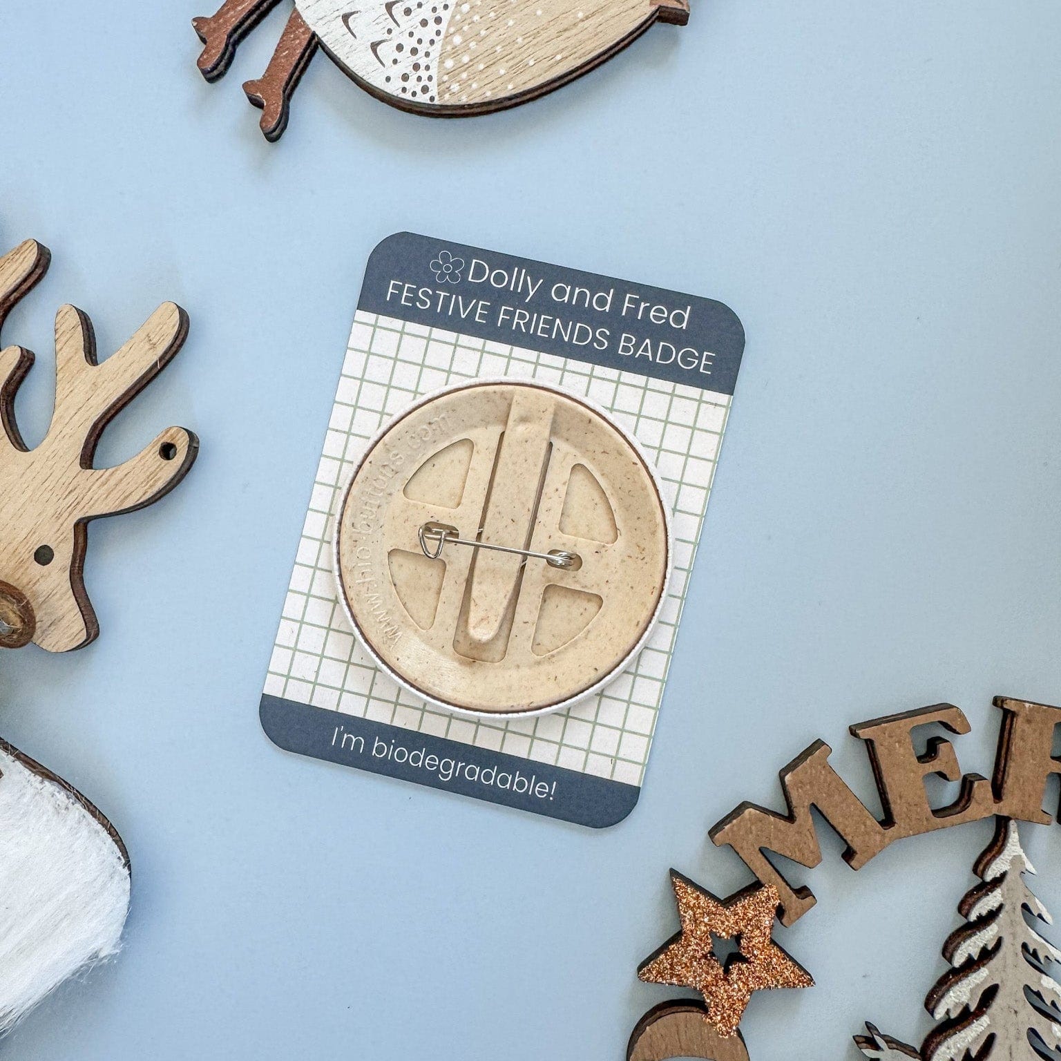 Baco of a biodegradable pin badge on a blue background, surrounded by festive decorations.