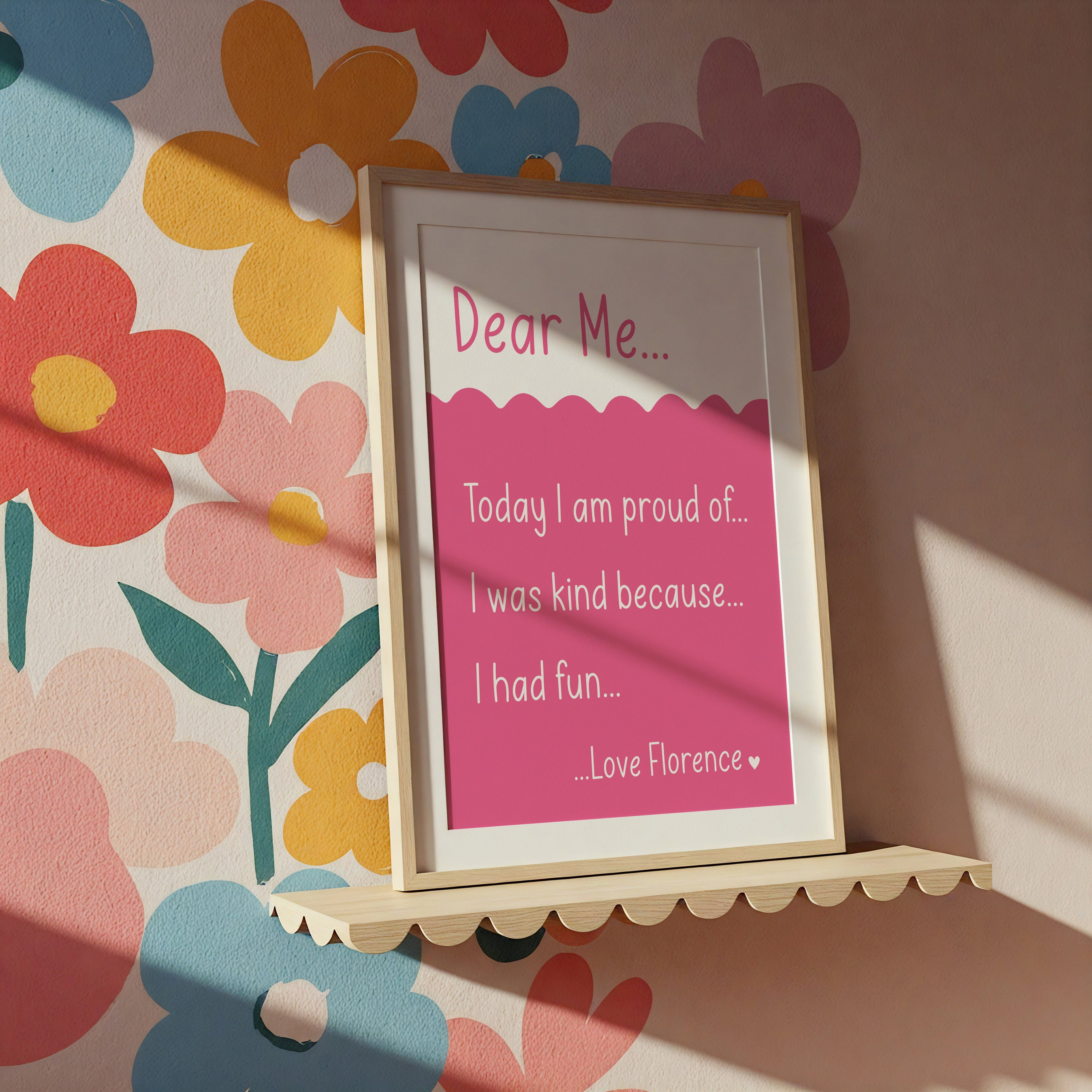Bright pink 'Dear Me' print in a white frame, styled against a colourful floral wallpaper background.
