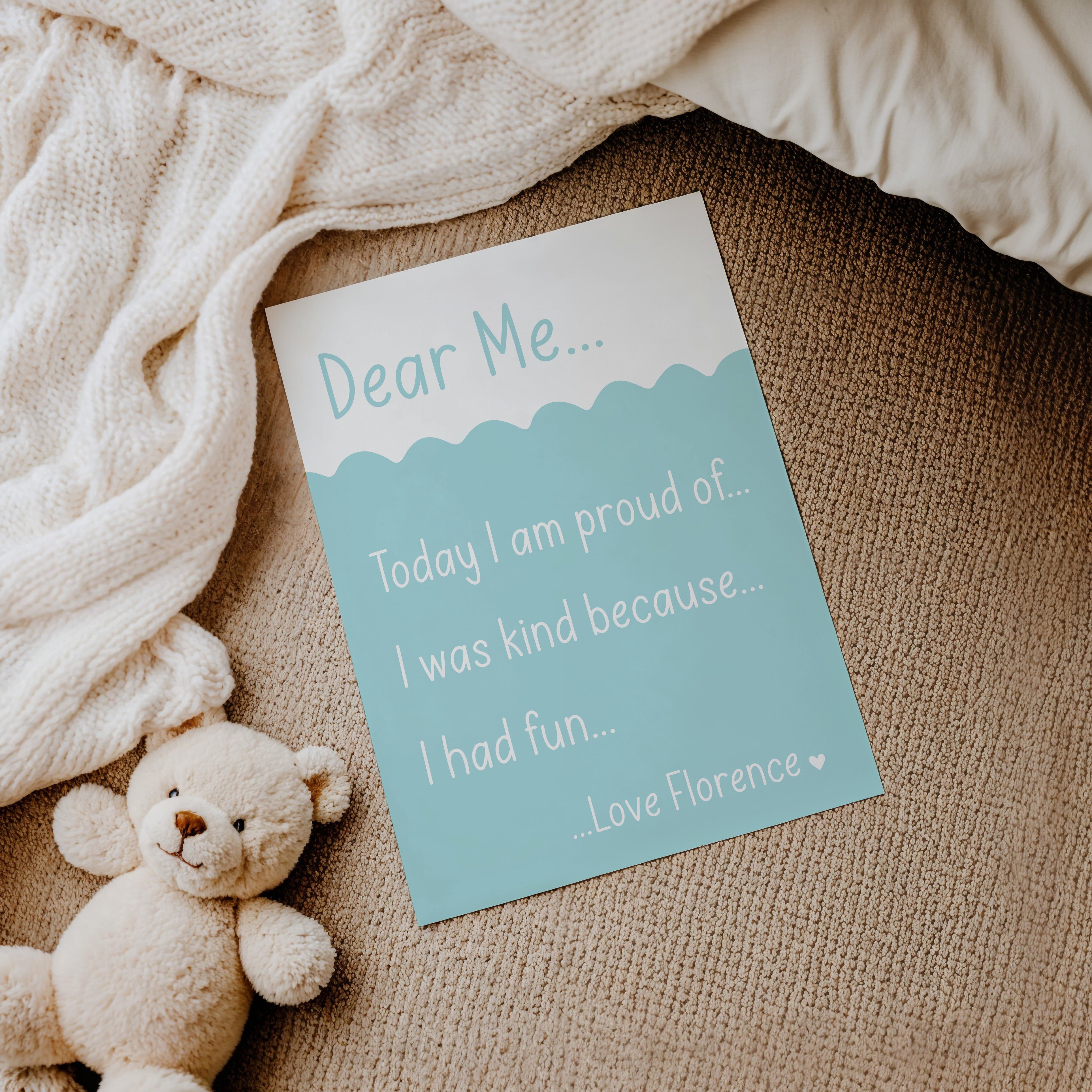 Teal version of the 'Dear Me' affirmation print laid on a cosy cream blanket with a soft toy nearby.