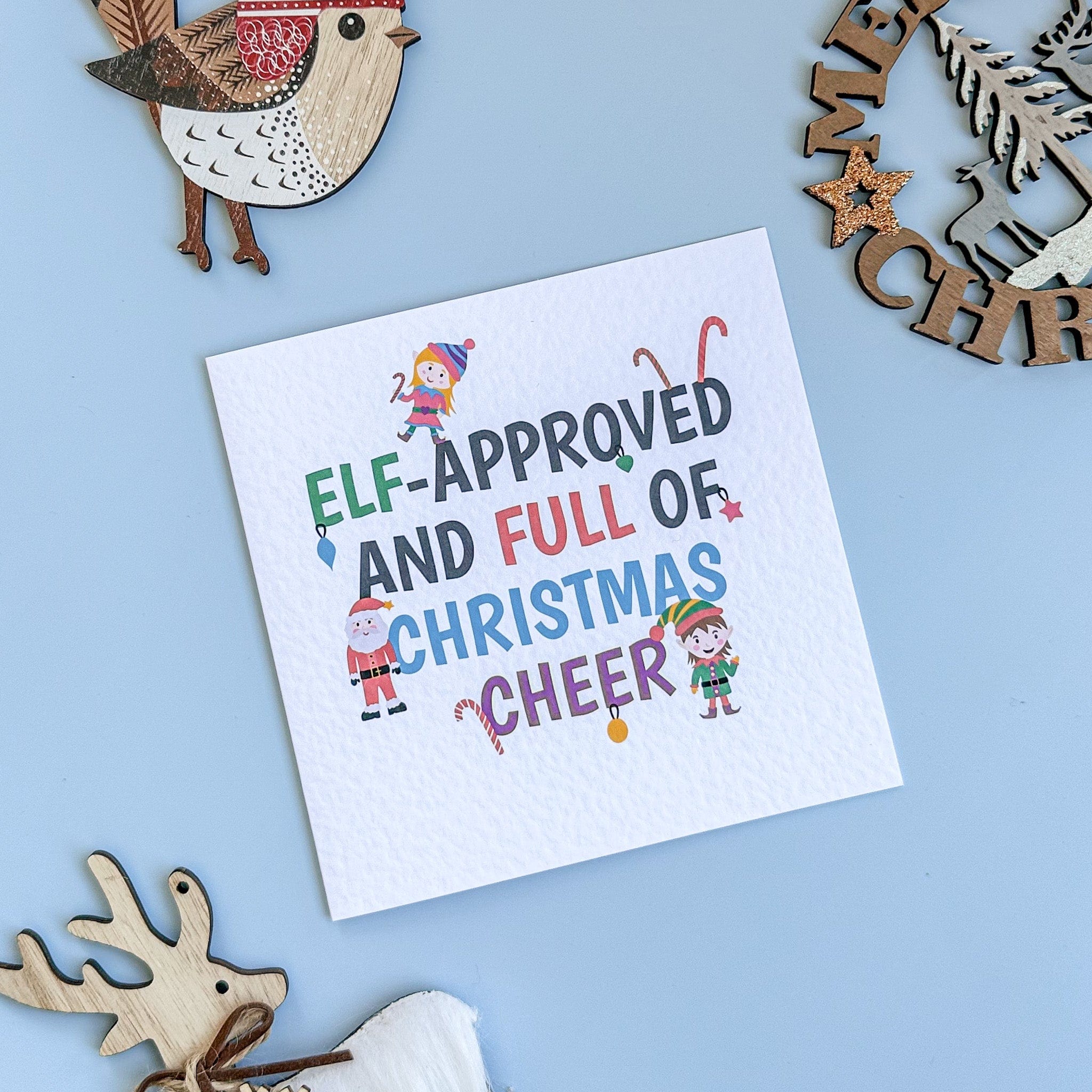 Christmas-themed card with 'Elf-Approved and Full of Christmas Cheer' text on a blue background with decorative elements.