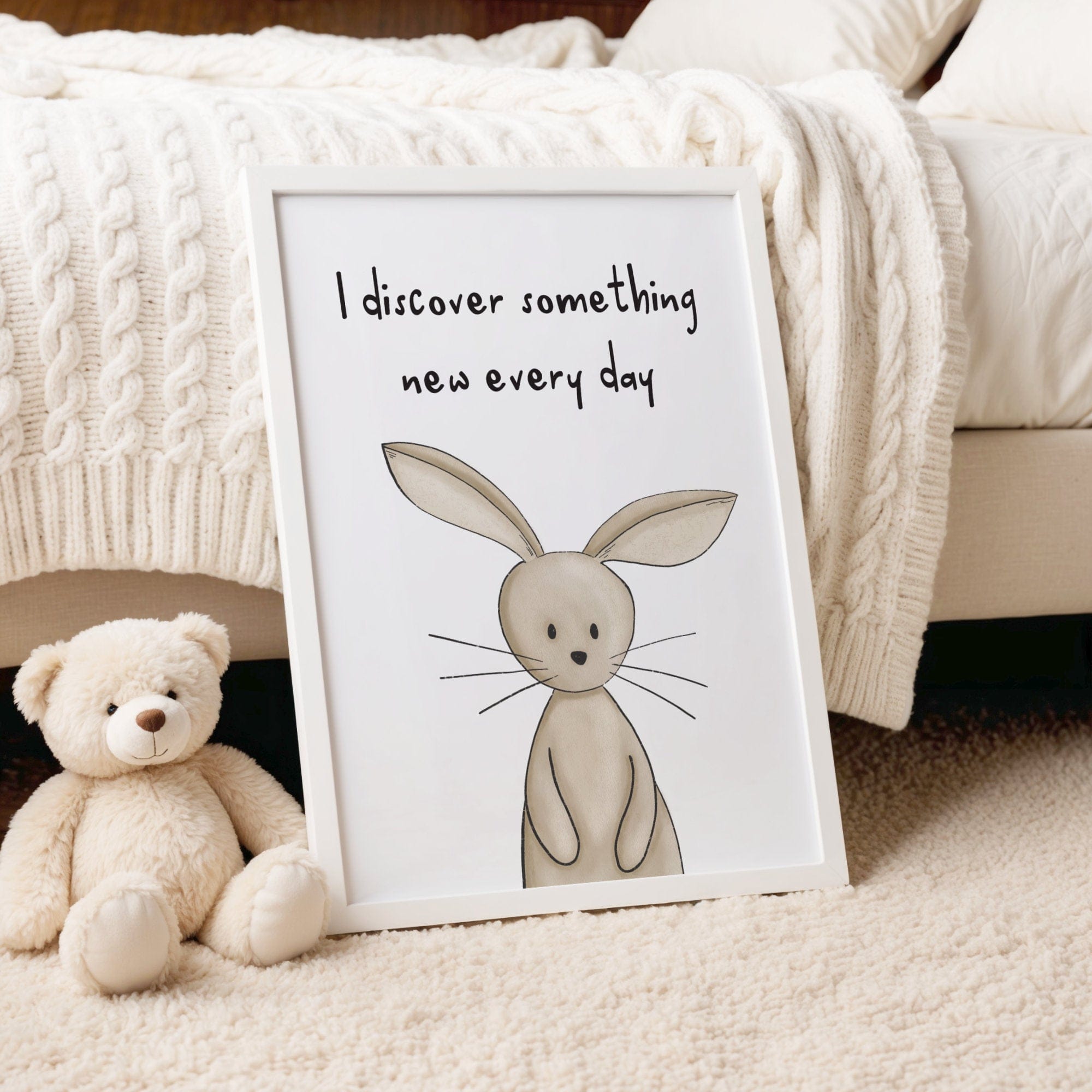 Framed illustration of a rabbit with text 'I discover something new every day' next to a teddy bear on a soft surface.