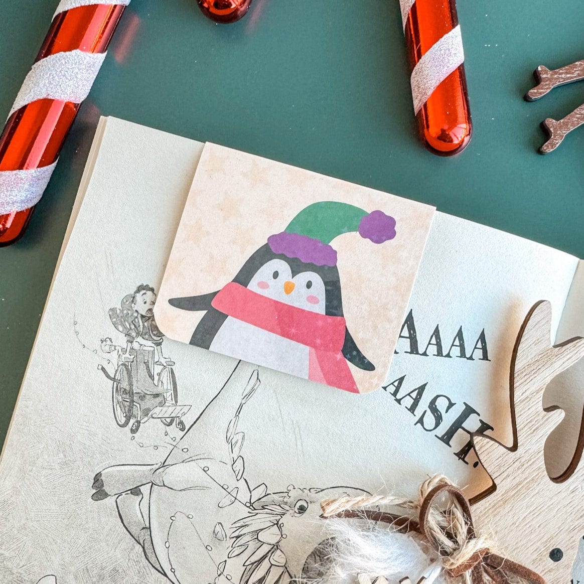 Holgraphic Penguin Bookmark on a book surrounded by Christmas Decorations
