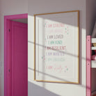 Personalised affirmation print in a pink-walled room with sunlight, showing its vibrant colors and framed in pink.