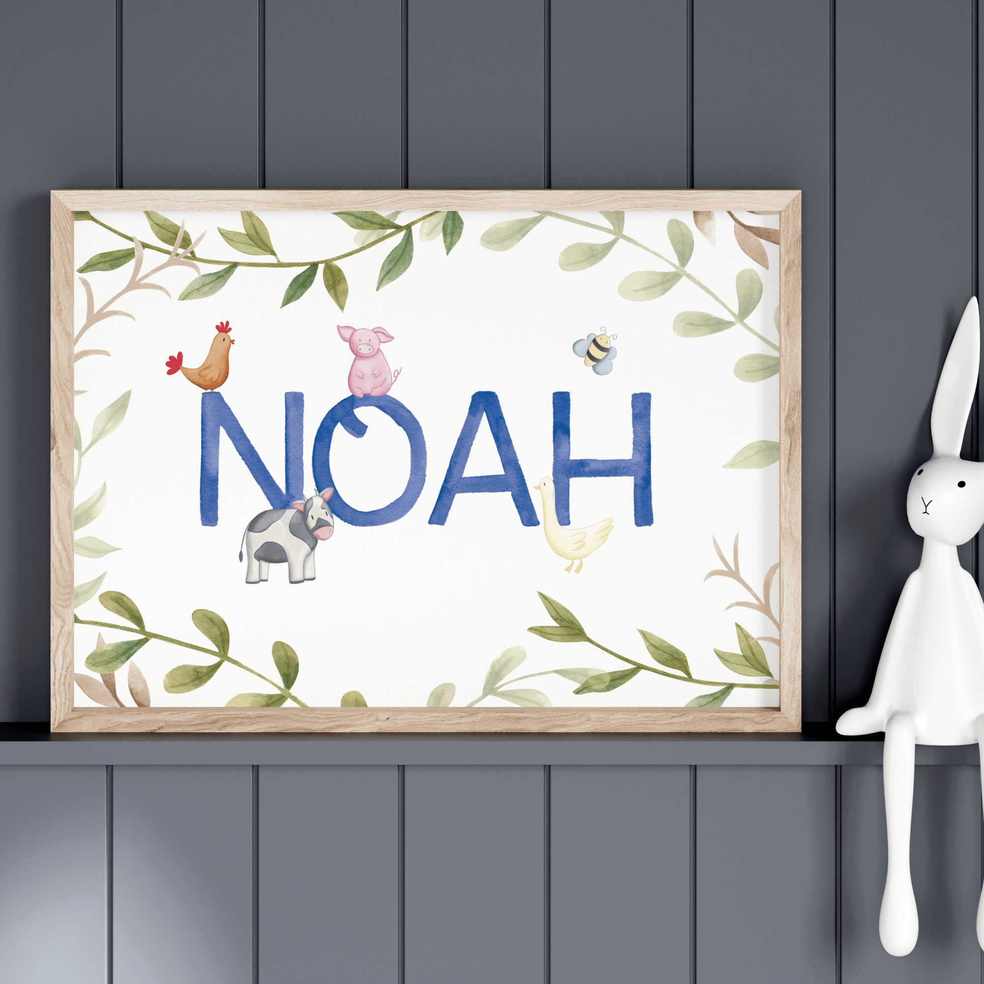 Framed artwork with 'NOAH' and farm animals on a dark gray wall with a white rabbit figurine.