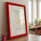 Single personalised "I AM" affirmation print from the dinosaur set in a red bobble frame, next to shelves of toys.