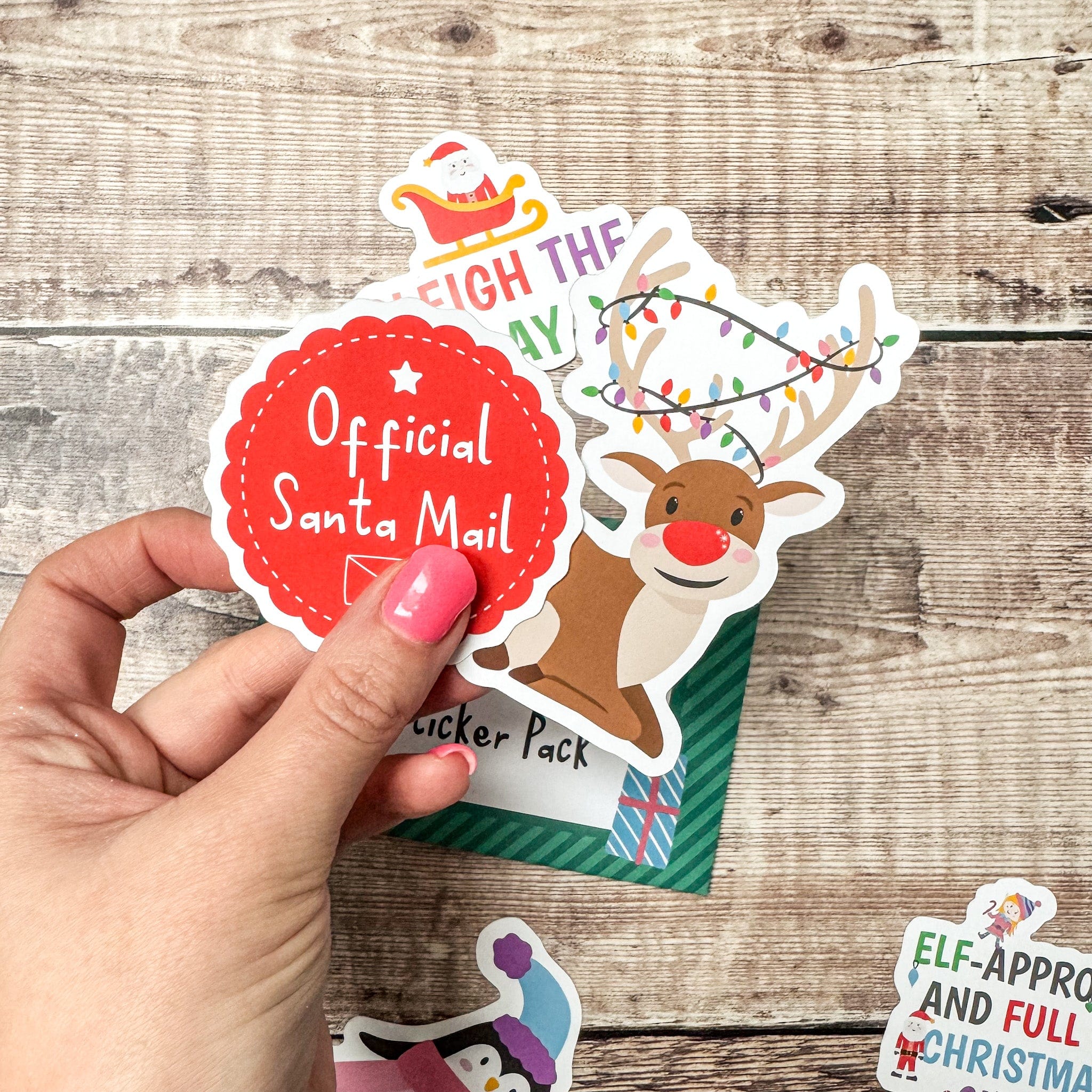 Hand holding reindeer and santa mail die cut stickers on a wooden background