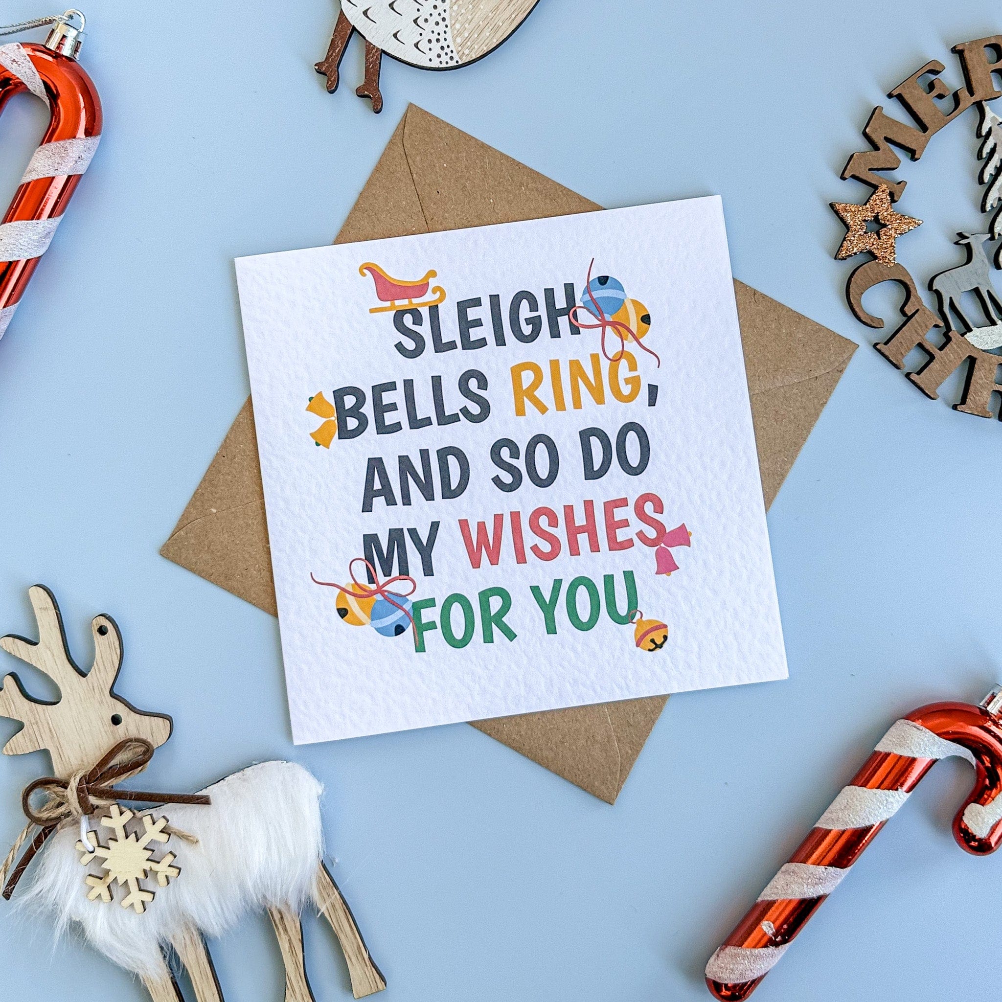 Christmas card with text 'Sleigh bells ring, and so do my wishes for you' surrounded by festive decorations on a blue background.