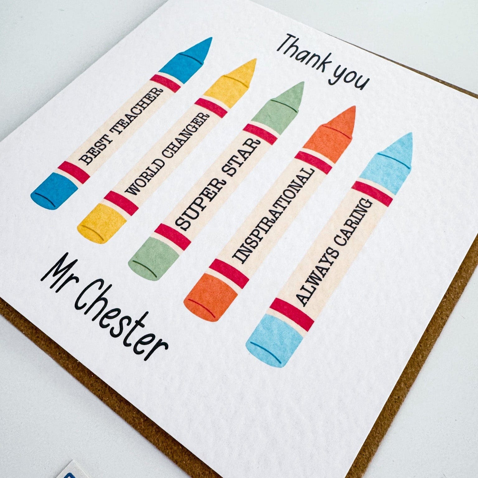 Flatlay image of a personalised teacher thank you card with colourful crayon design and "Mr Chester" on the front, paired with a brown envelope – a thoughtful end-of-term gift for teachers.