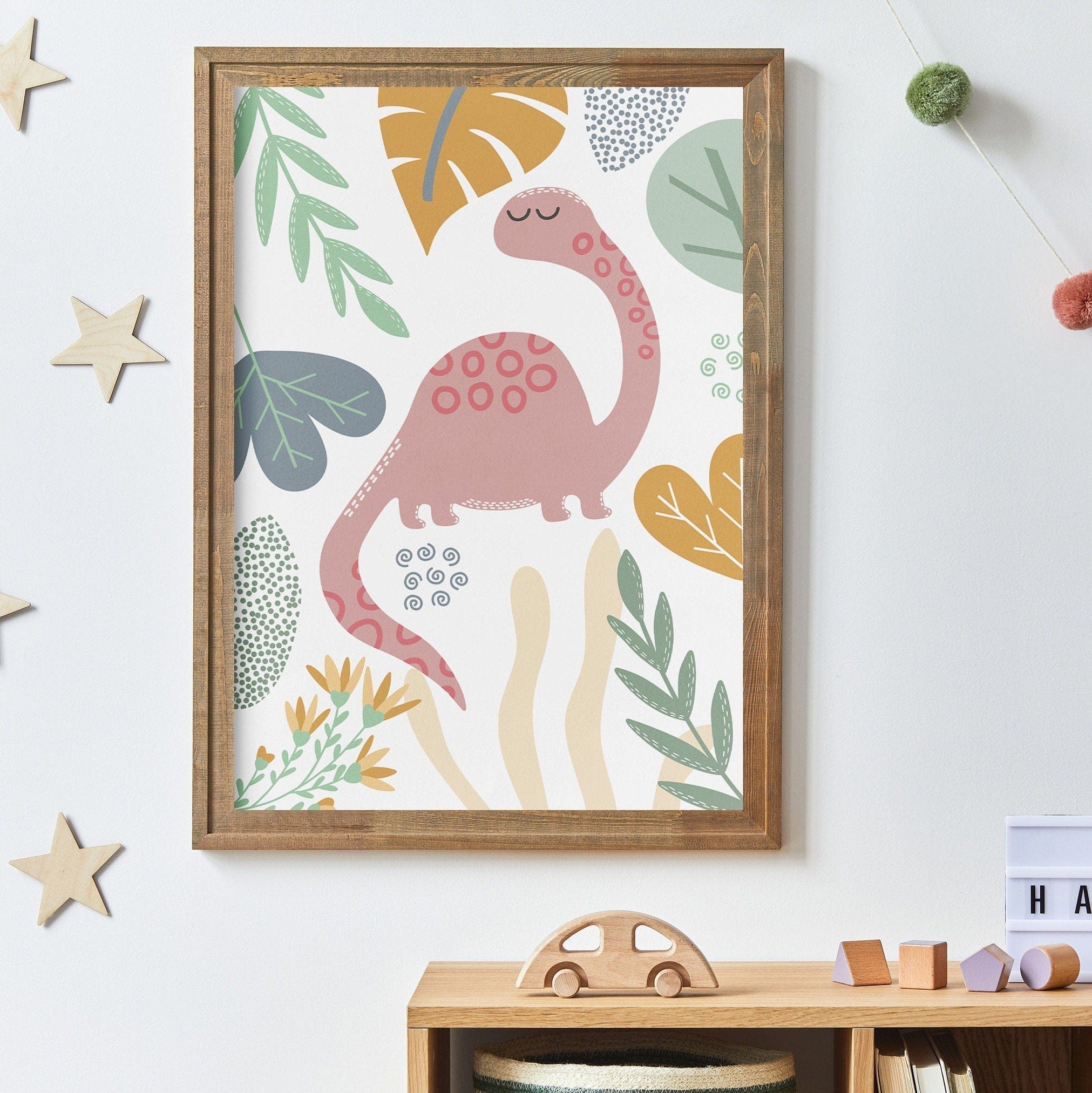 Framed children's poster with a pink dinosaur and leaves on a white wall.