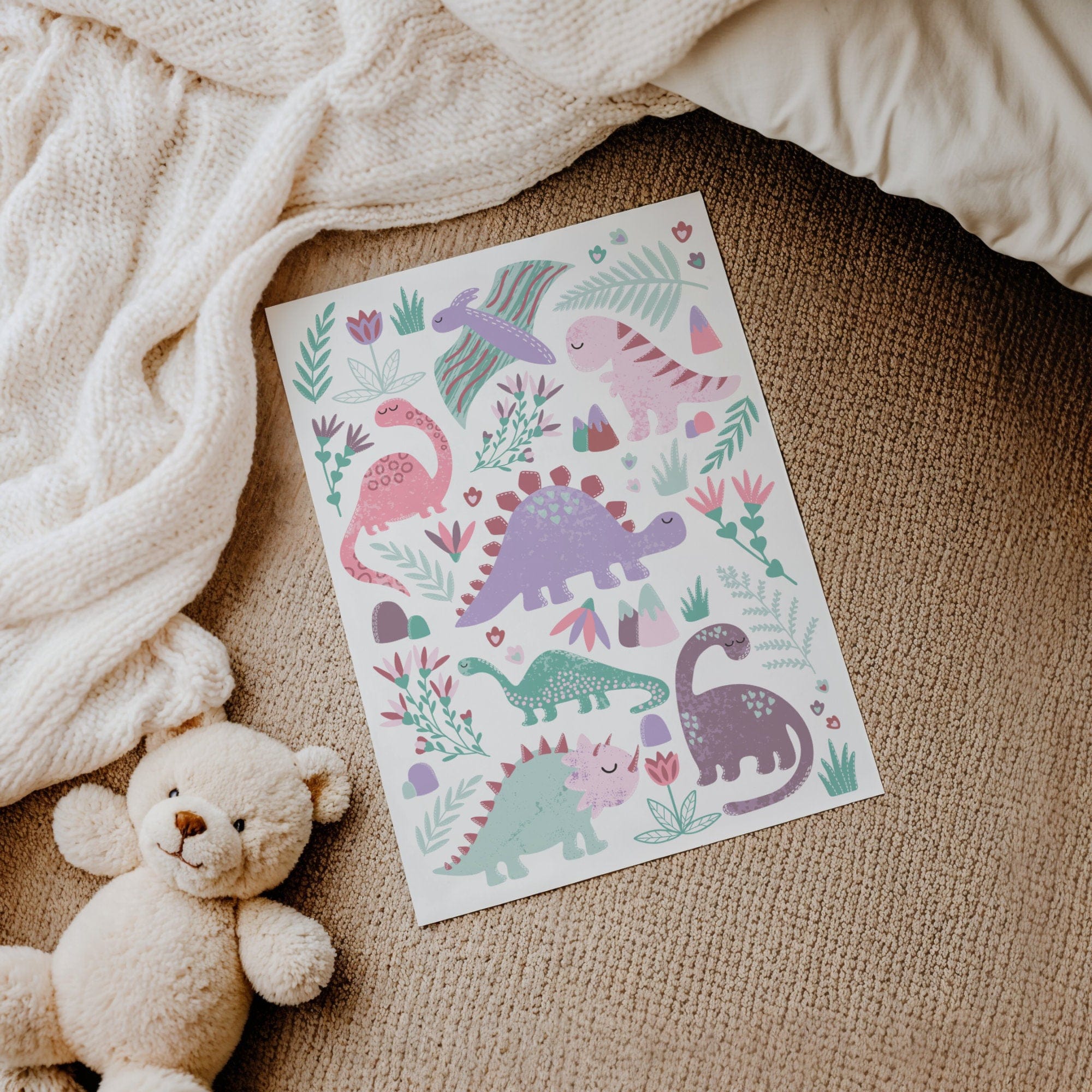 A personalised dinosaur print on a textured surface with a teddy bear and blanket.