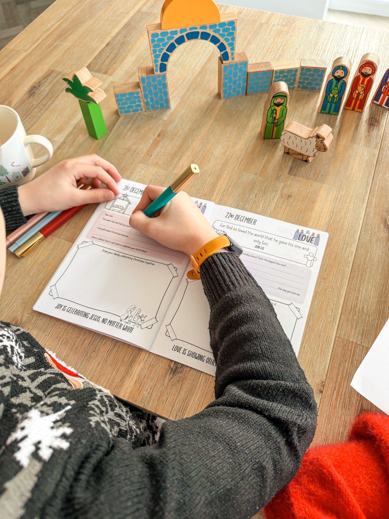 A child filling in his advent journal surrounded by a wooden nativity scene
