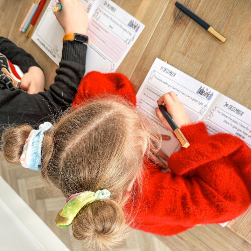 Two children sitting at a wooden table with their Advent prayer journals