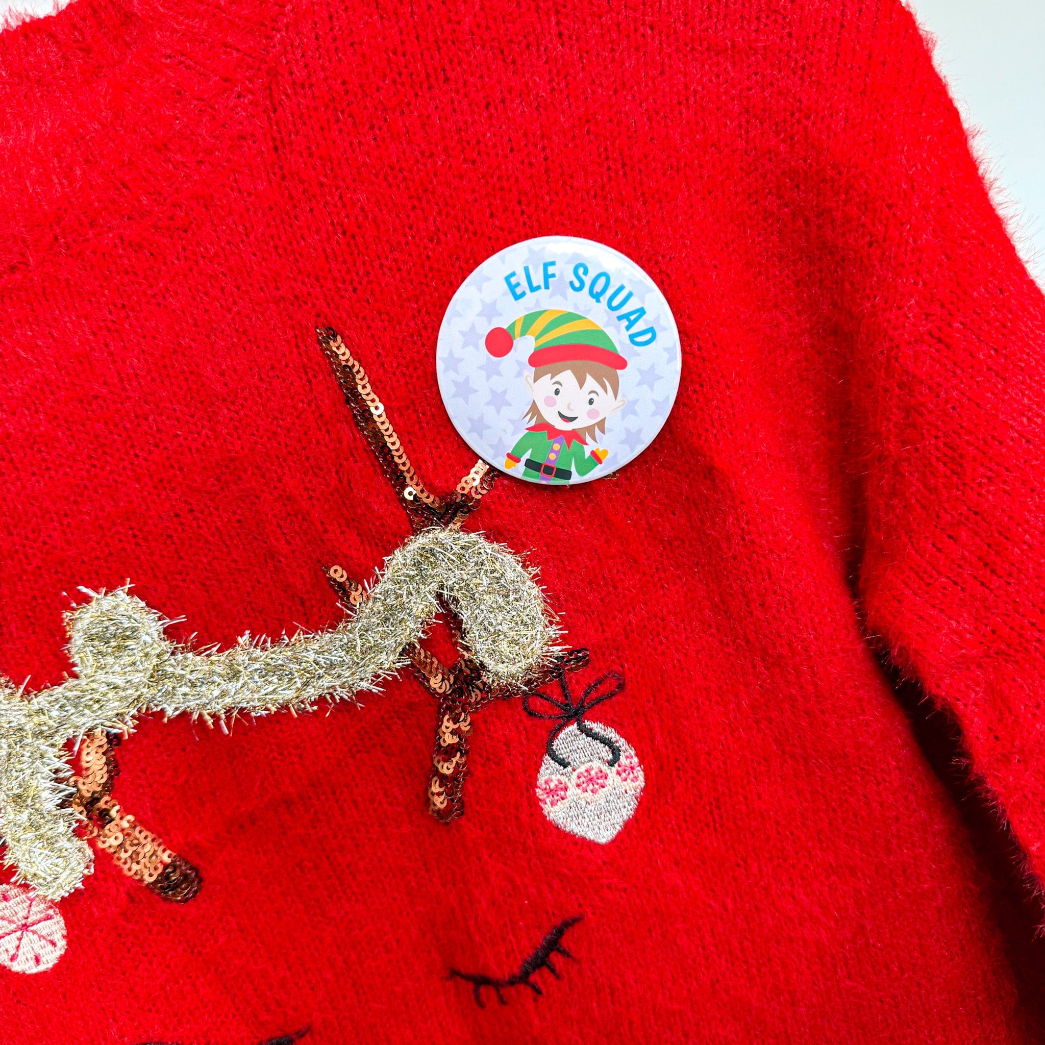 Red sweater with gold reindeer and 'Elf Squad' button badge on a white background