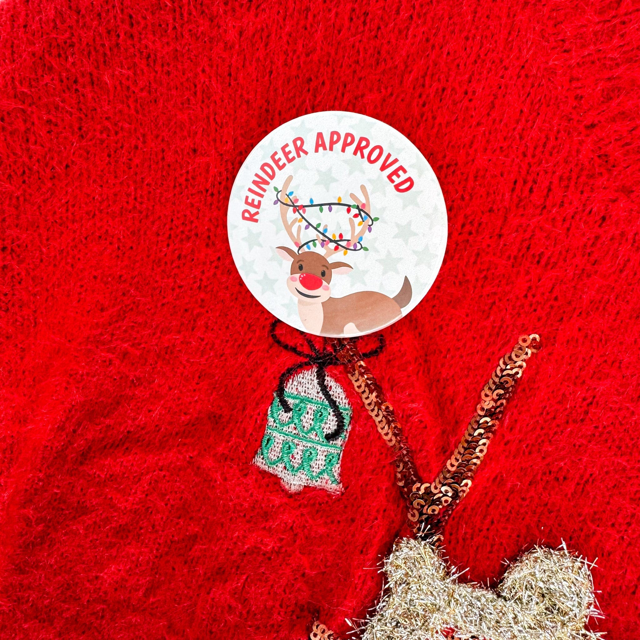 Decorative reindeer button badge with 'Reindeer Approved' label on a red Christmas jumper