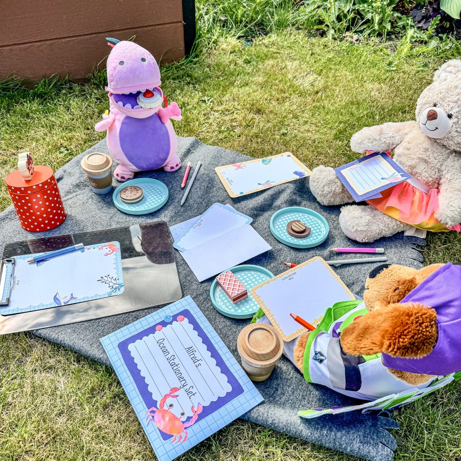 A picnic blanket with teddy bears enjoying a picnic in the garden while doing some collouring using an ocean writing set