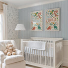 Nursery room with a crib, chair, teddy bear, and dinosaur wall art with names and dinosaurs.