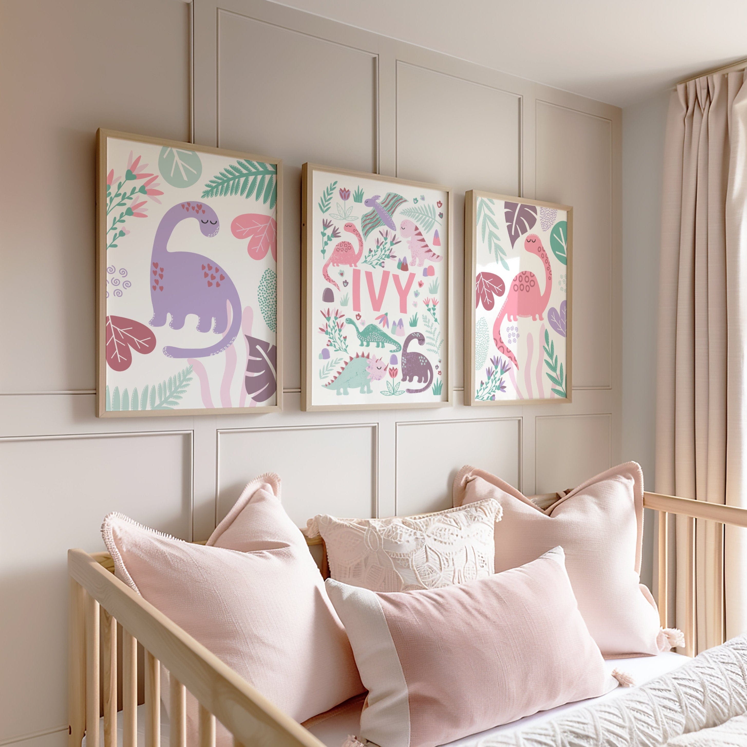 Children's room with framed illustrations of dinosaurs and the name 'IVY' on a wall above a bed with pink pillows.