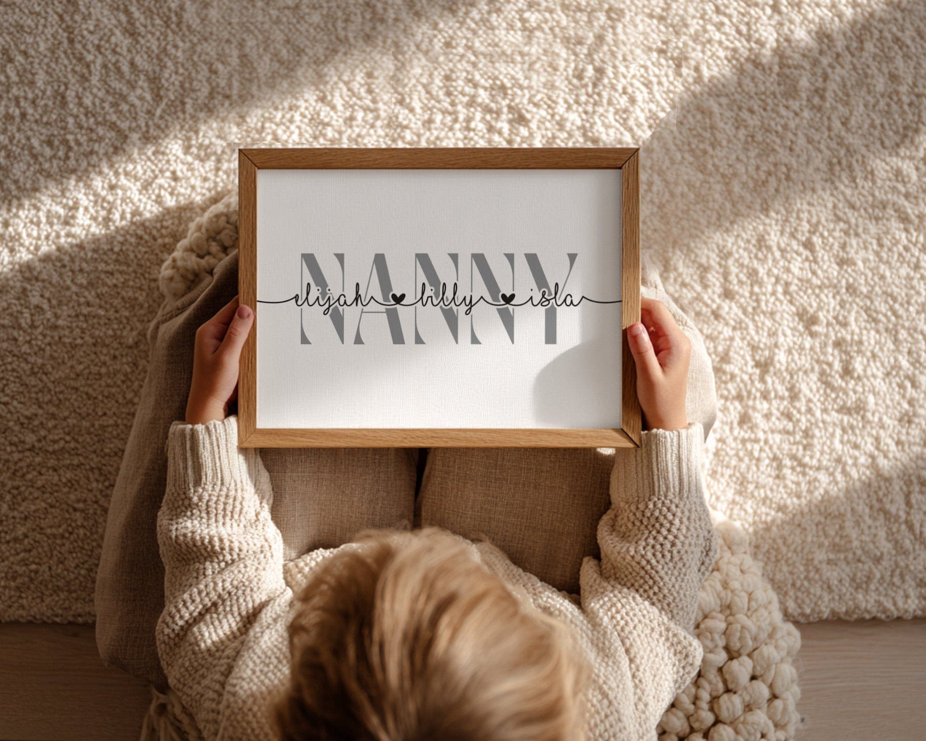 A child holding a framed print with the word nanny and childrens names. 