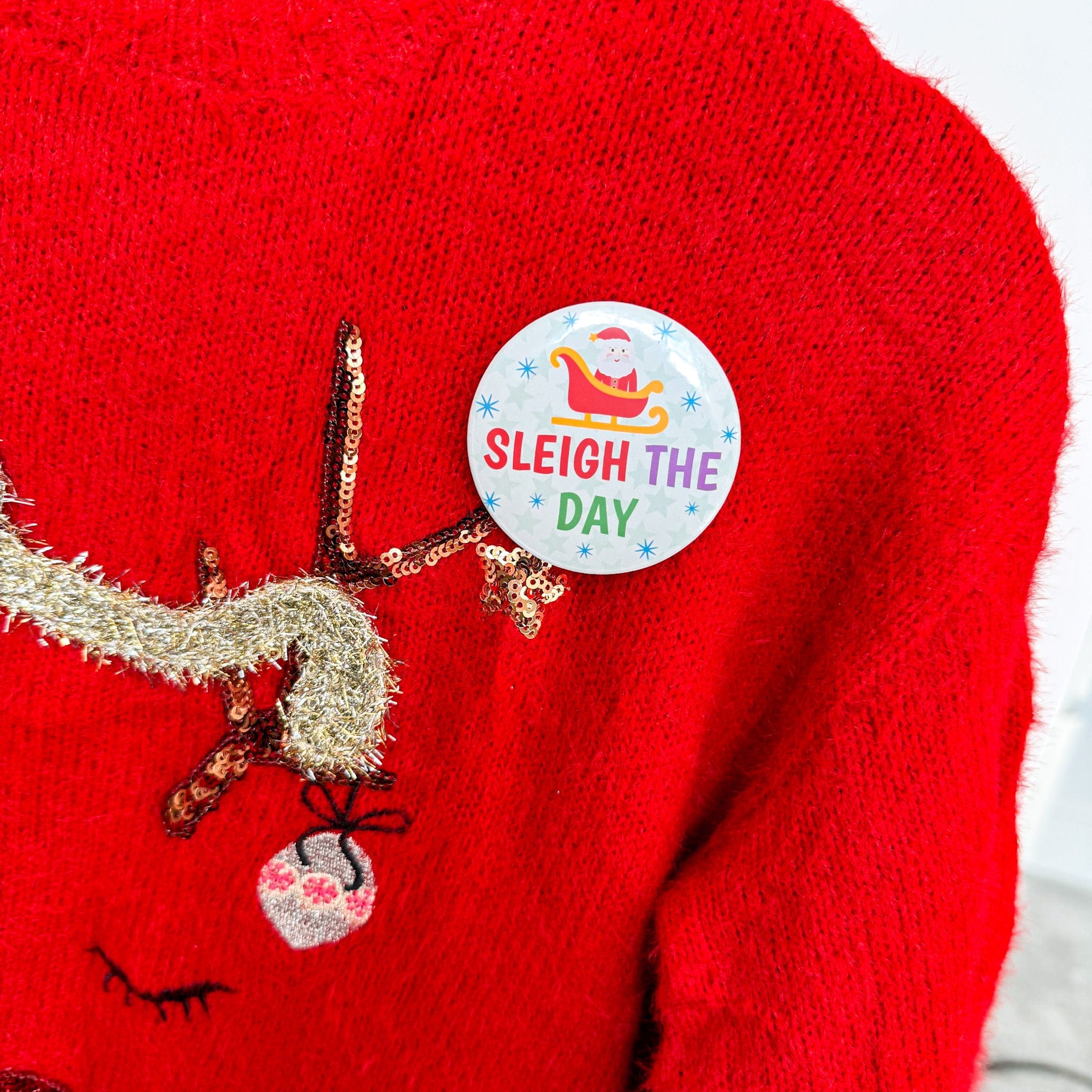 Christmas jumper with reindeer design and 'Sleigh the Day' button badge